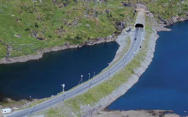 dronebilde av veien som kommer ut av en tunnel fra et fjell, med vann på hver side.