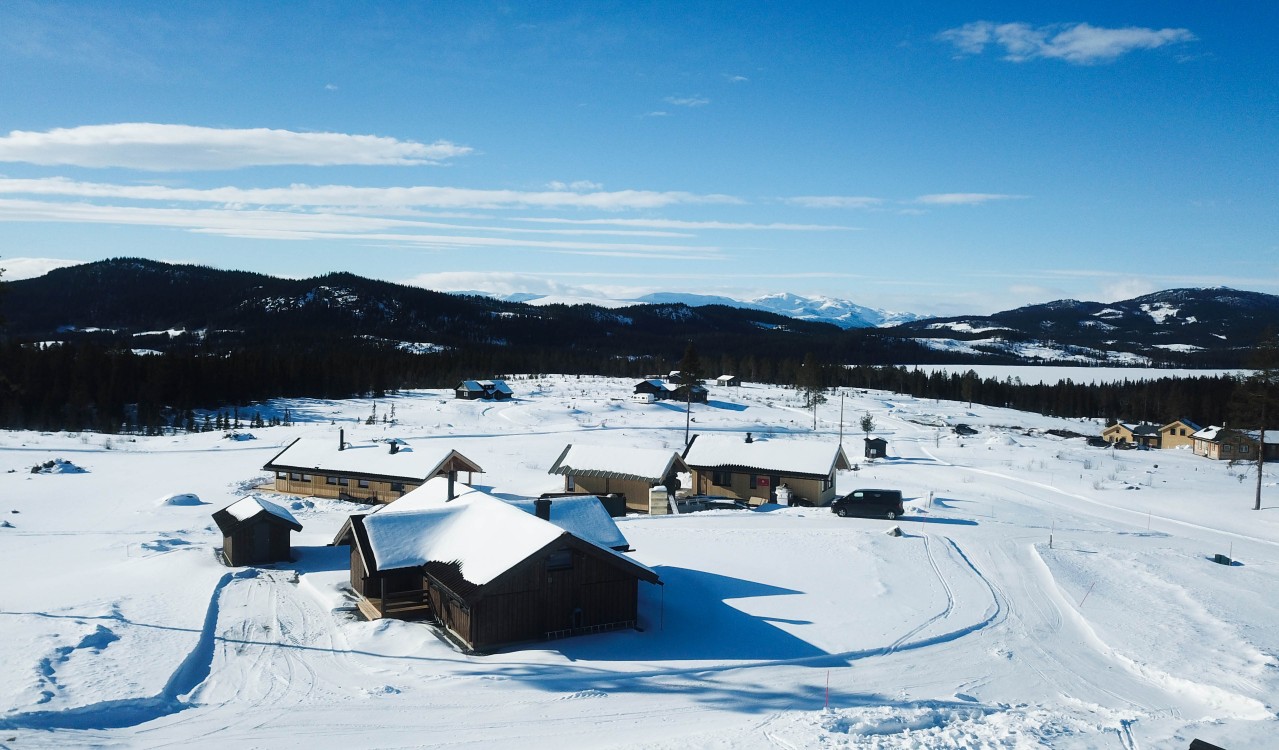 Oversiktsbilde av snødekket hyttelandskap på fjellet med sol og blå himmel.