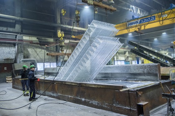 på innsiden av stor produksjonshall og en mannlig arbeider som manøvrerer maskin som heiser pall med metallstiger.