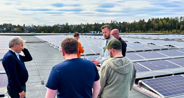 seks menn står på stort flatt tak med solcellepaneler og prater.