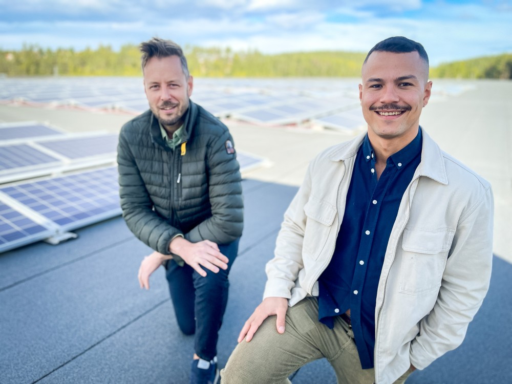 to unge menn står på tak dekket med solcellepaneler og smiler til kamera.