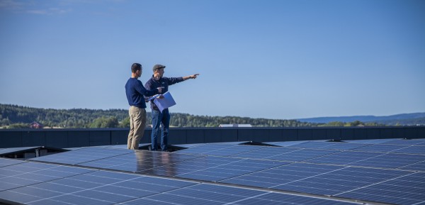 to menn står på tak dekket med solcellepaneler.