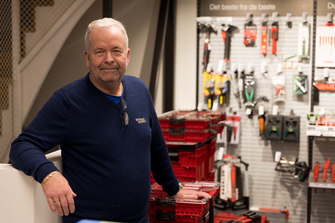 Mann med grått hår og Berggård Amundsen-genser står foran store verktøykasser inne i en elektrikerbutikk