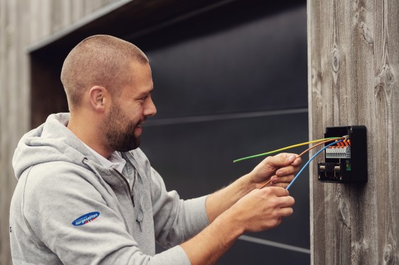 ung mannlig elektriker monterer veggfeste til elbillader på husvegg ved siden av garasjeport.