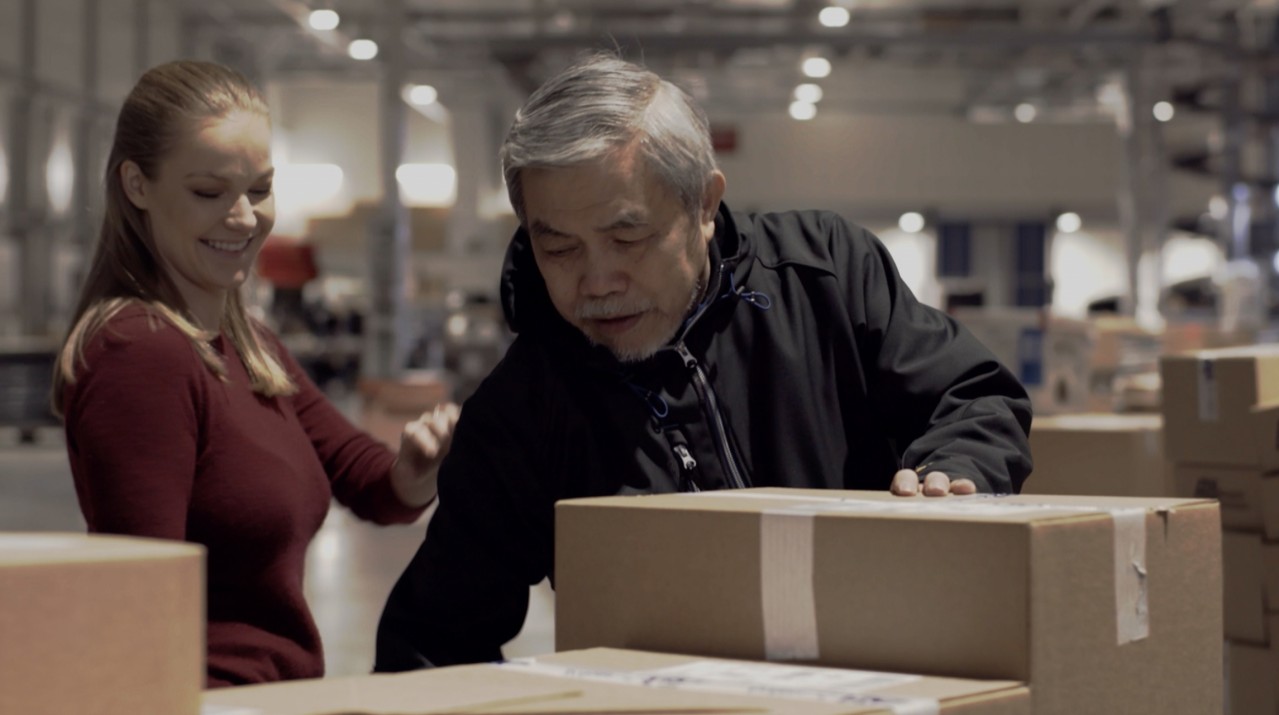 en eldre mann og ung kvinne står på et lager og håndterer pappesker.